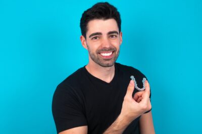 Man wearing black shirt holding aligners on blue background